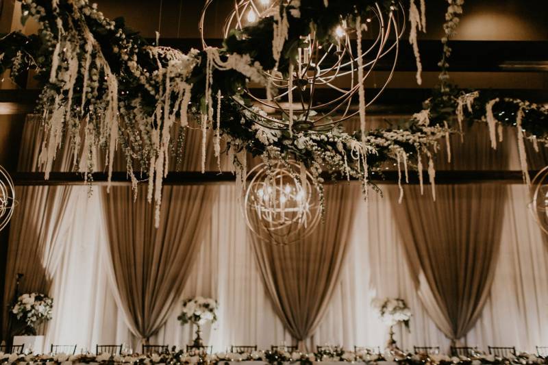 Tables set up around room underneath large round chandeliers and draping fabrics  