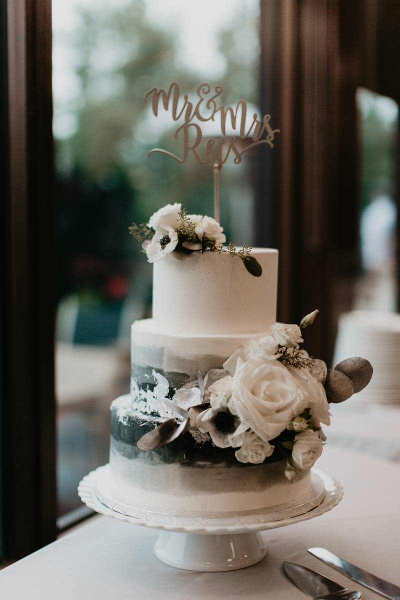Green and white wedding cake with white floral accents on white table 