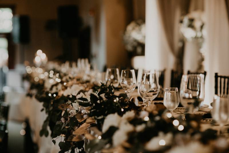 Long table with green table runner and empty wine glasses along it 