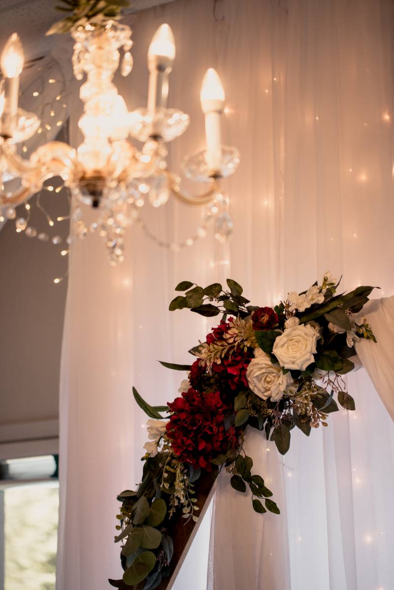 Burgundy and white floral arrangement in front of large chandelier 