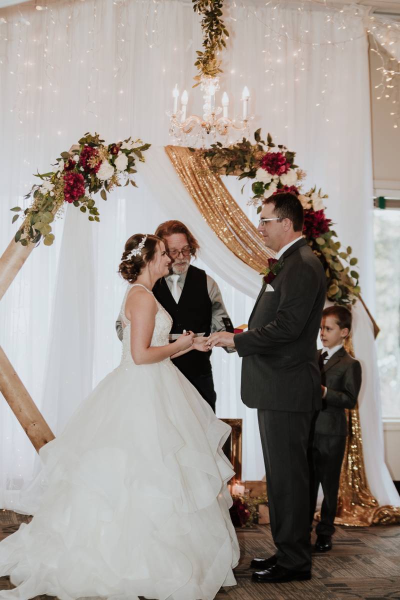 Bride and groom holding hands in front of wooden wedding arch and chandelier 