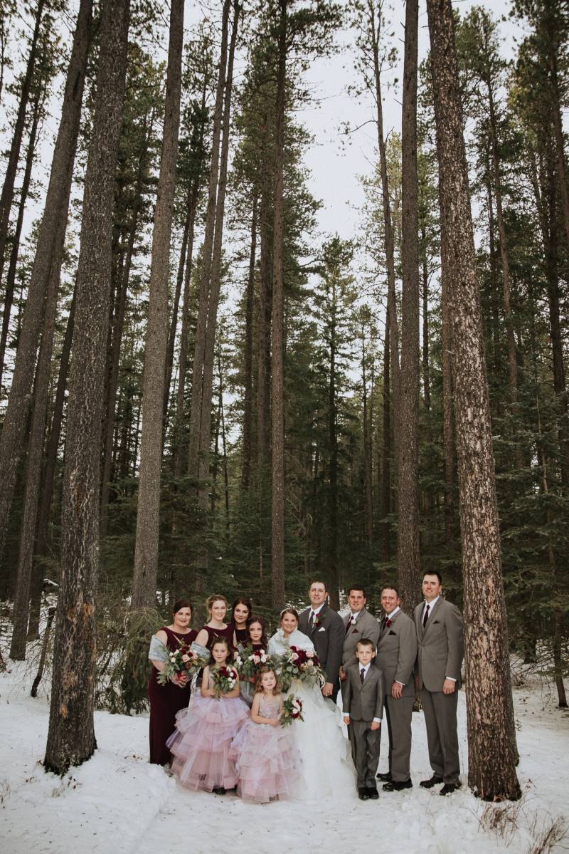 Groomsmen groom bride and bridesmaids stand together on snowy forest pathway