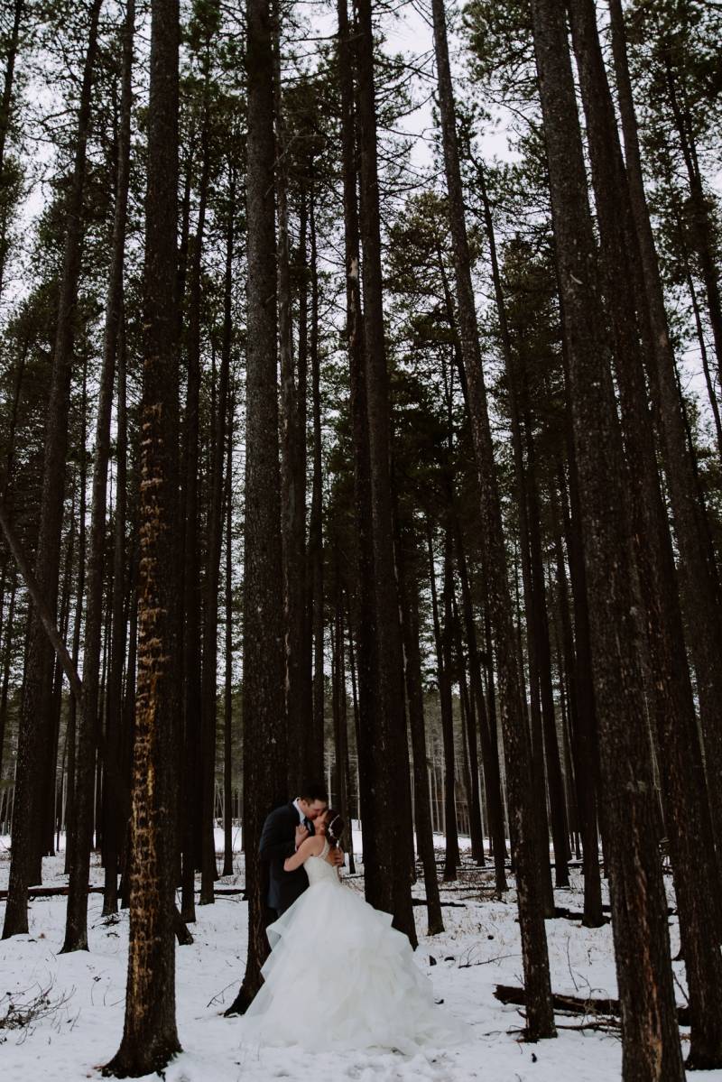 Bride and groom kiss embracing against tree in snowy forest