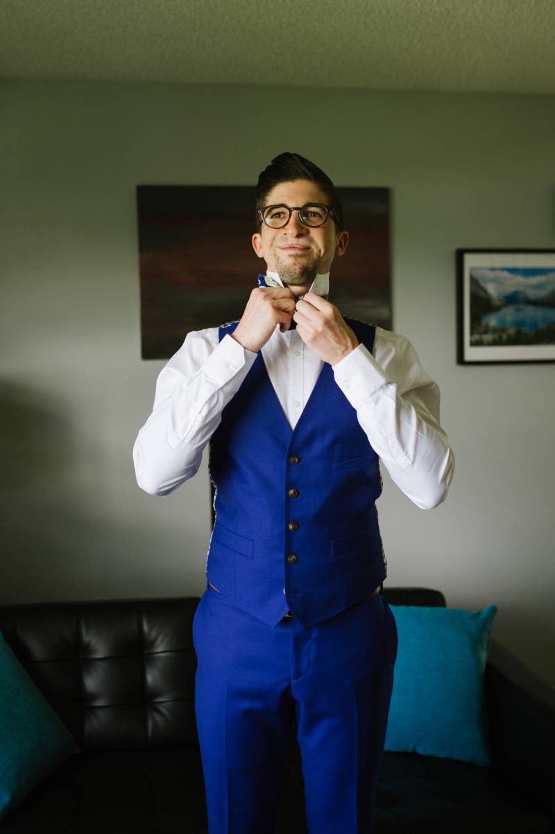 Man in blue suit adjusts bowtie while grinning 