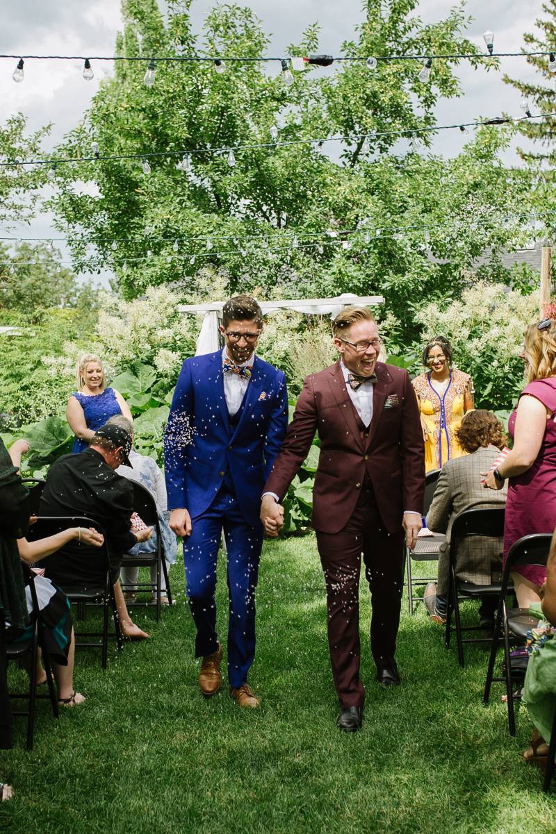 Grooms walking down the aisle holding hands smiling confetti