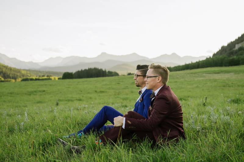 Grooms sitting smiling in large open grassy field