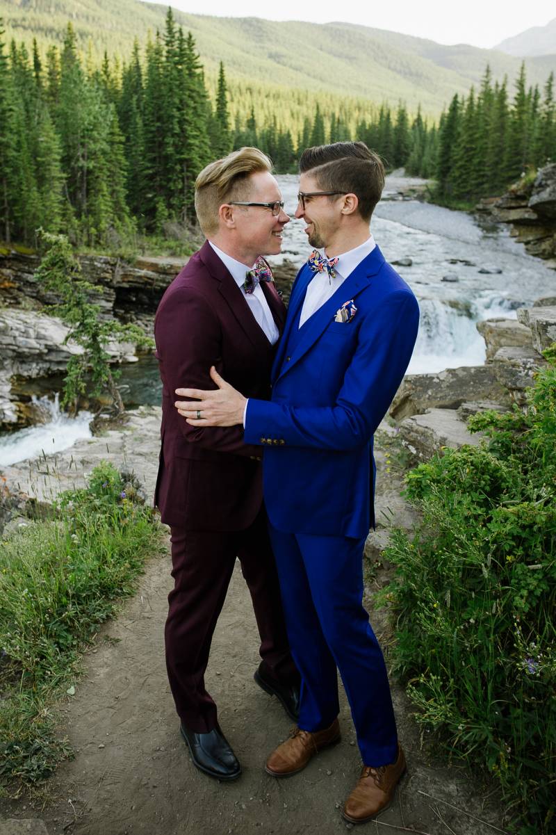 Grooms smiling embraced on river pathway 