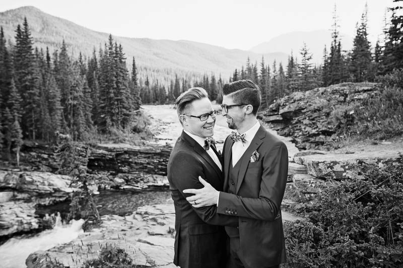 Grooms embrace in front of riverbank