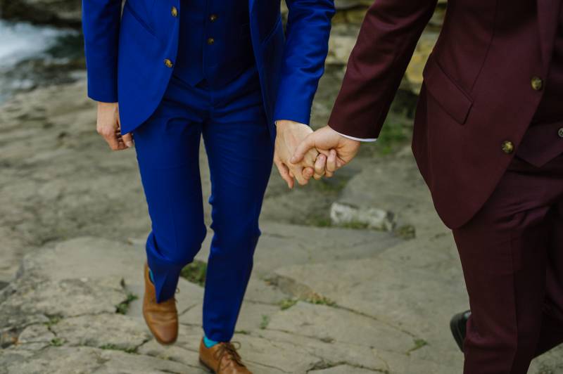 Grooms holding hands walking up riverbank