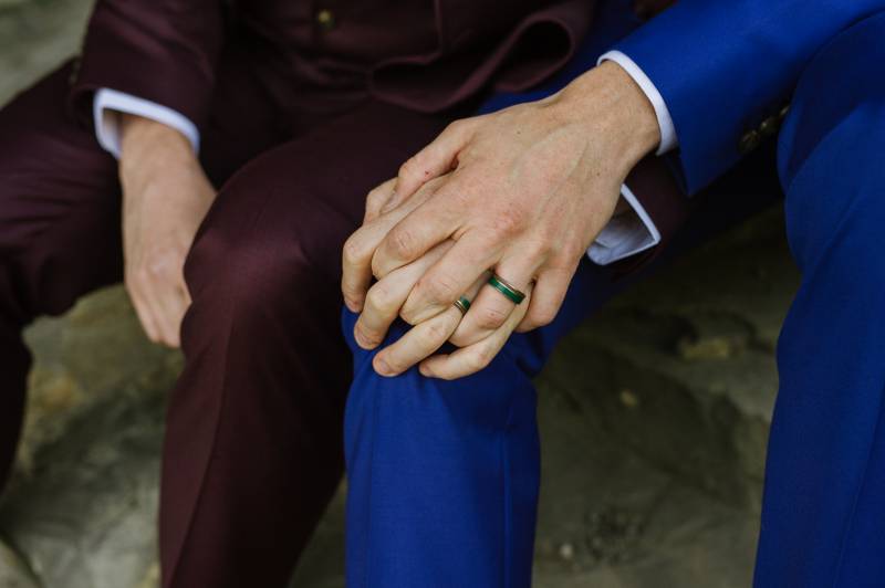 Hands of grooms rested on knee sitting on rocks