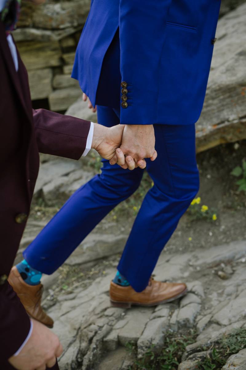 Grooms holding hands walking up rocky path