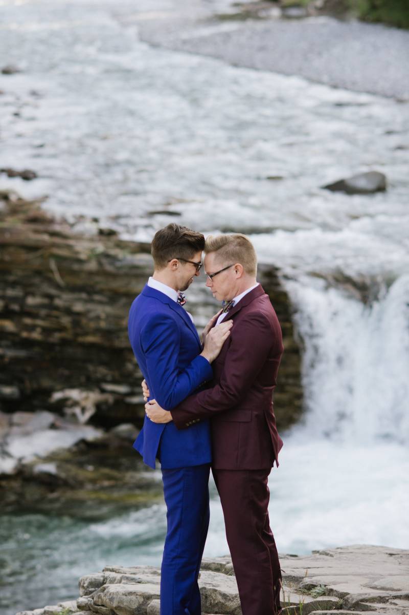 Grooms embrace touching foreheads with waterfall in background