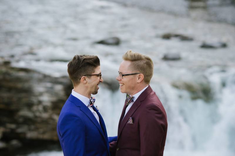 Grooms smiling in front of waterfall 
