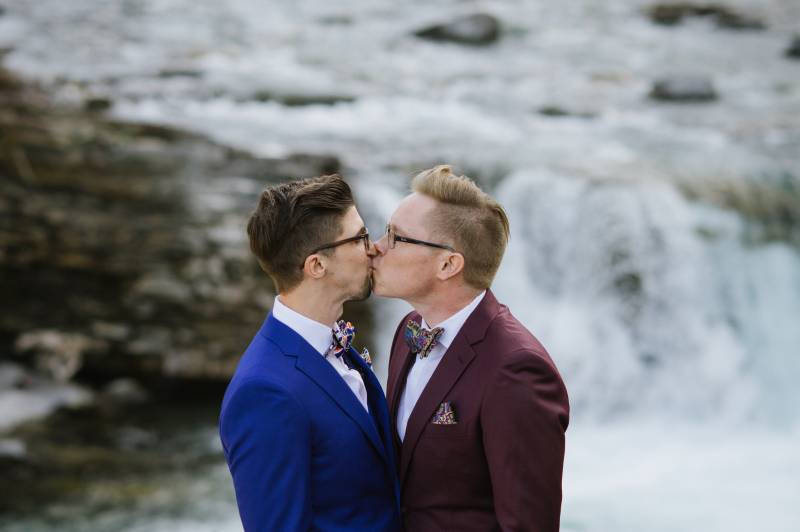 Grooms kiss in front of waterfall 