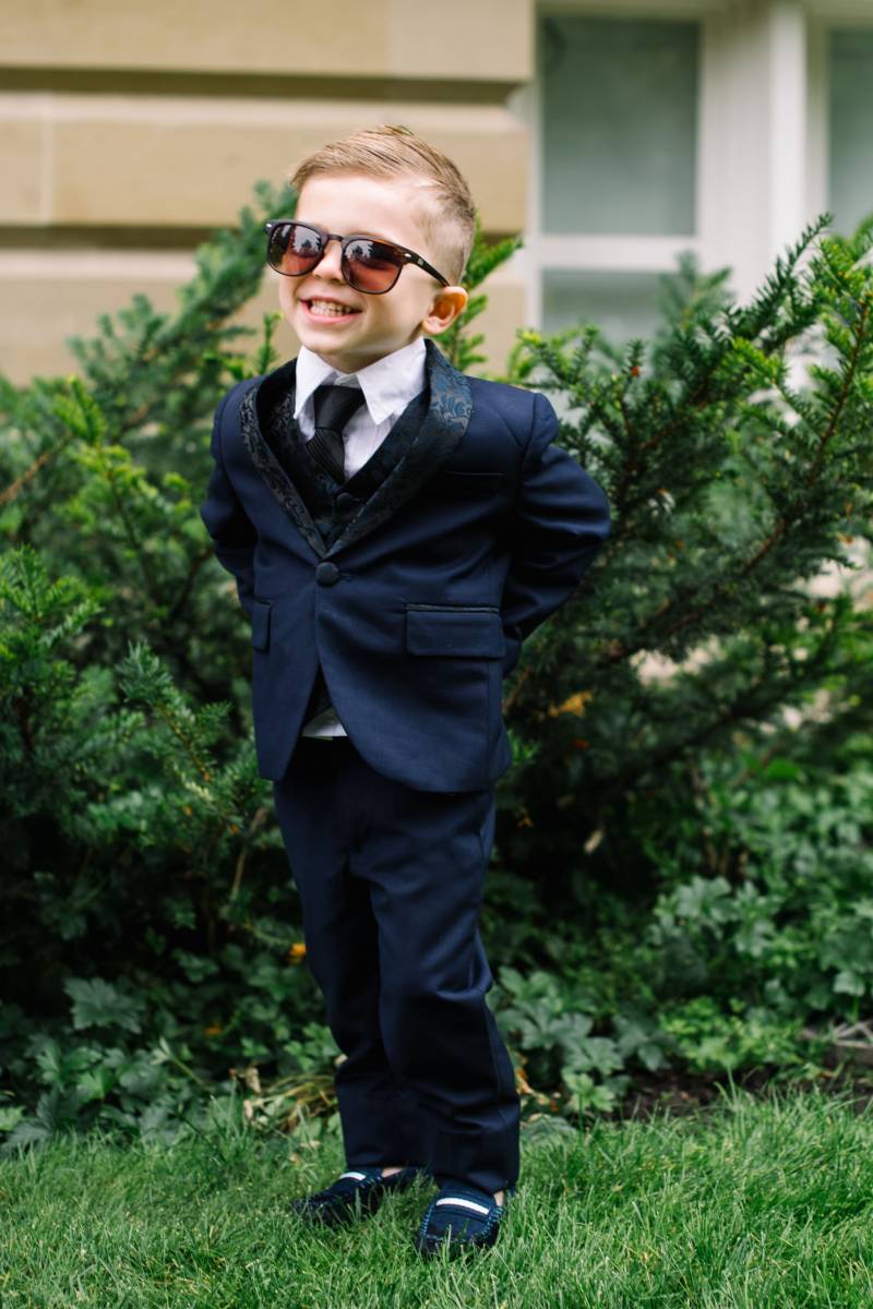 Child standing in grass wearing dark blue suit and sunglasses 