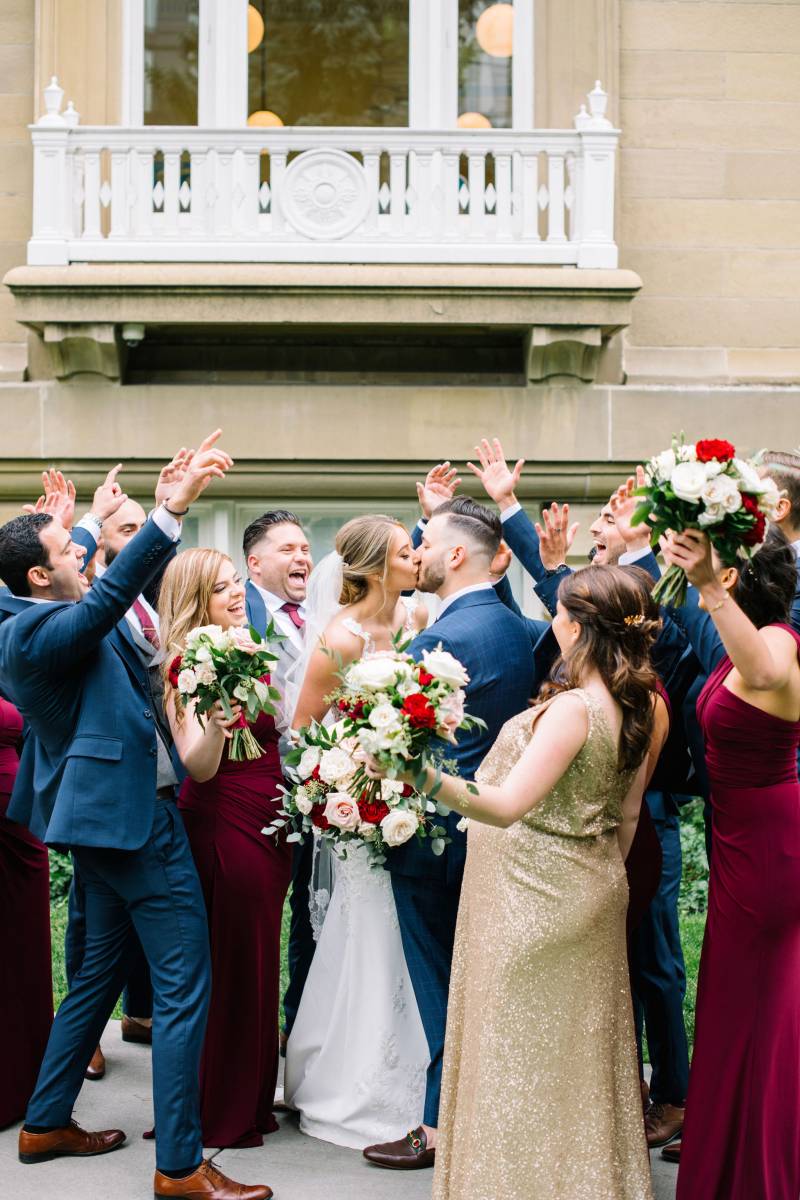 Bride and groom kiss while bridesmaids and groomsmen celebrate around them 
