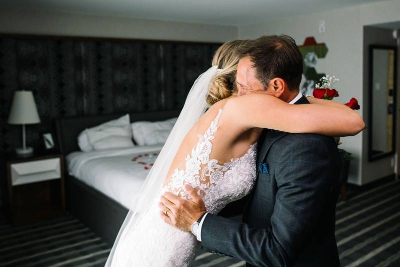 Bride in white lace bodice dress and white veil embrace man in grey suit 