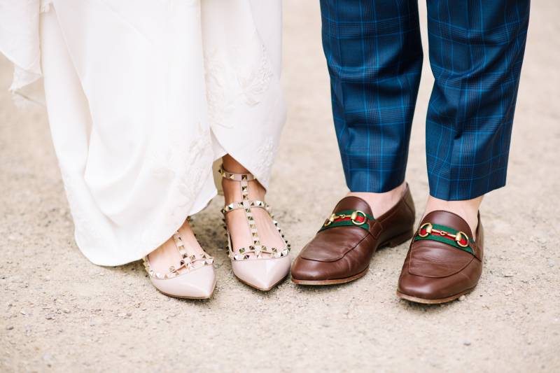 Bride wearing studded heels and groom wearing gucci slippers on dirt pathway