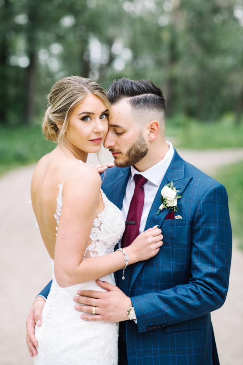 Bride in white lace dress embraced by groom in blue suit and burgundy tie 