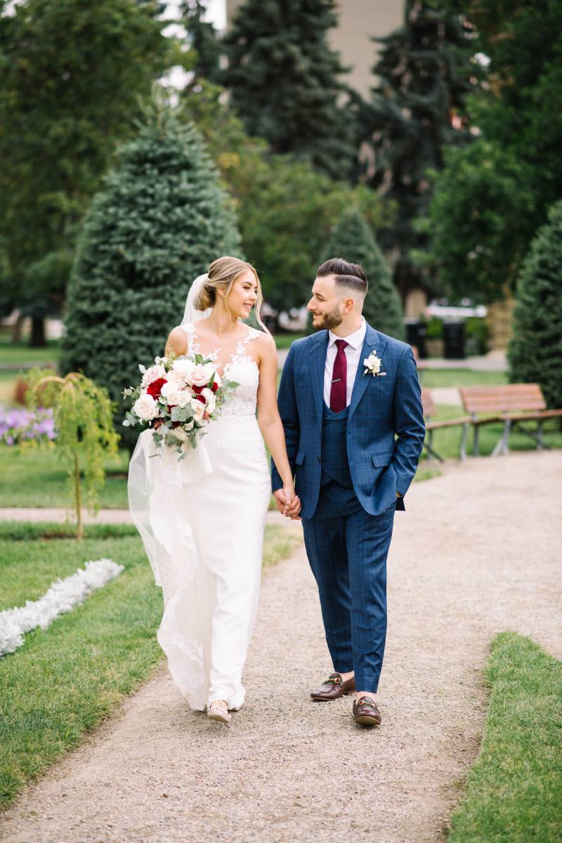 Bride and groom hold hands walking down green garden pathway 