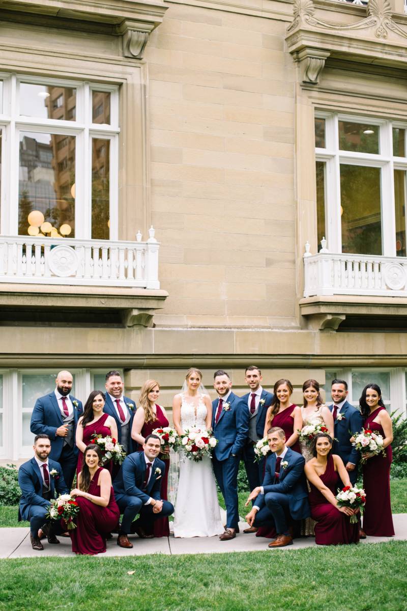 Bridesmaids and Groomsmen stand together in front of brown estate with white window frames