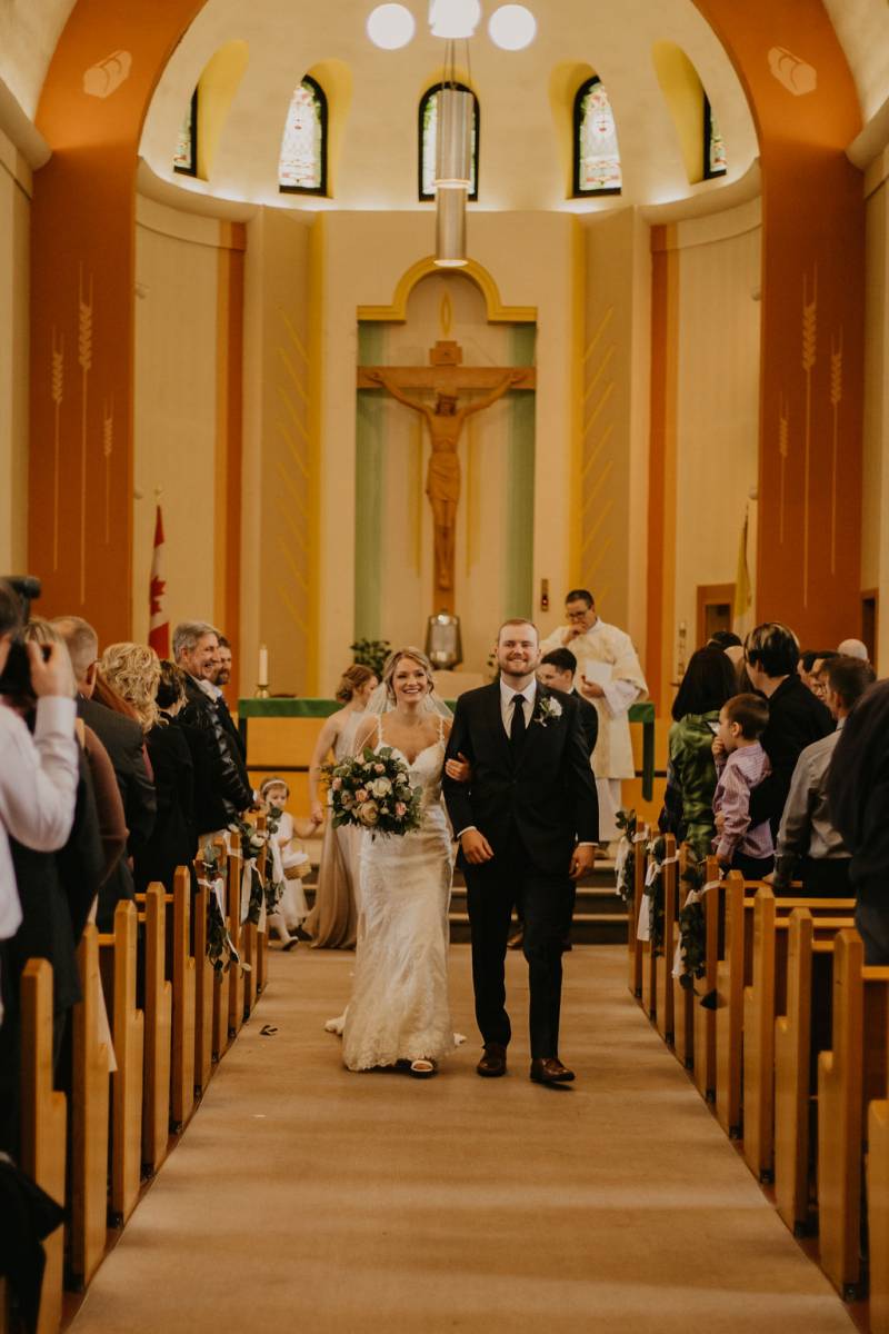 Man and woman walk linking arms down church aisle smiling 