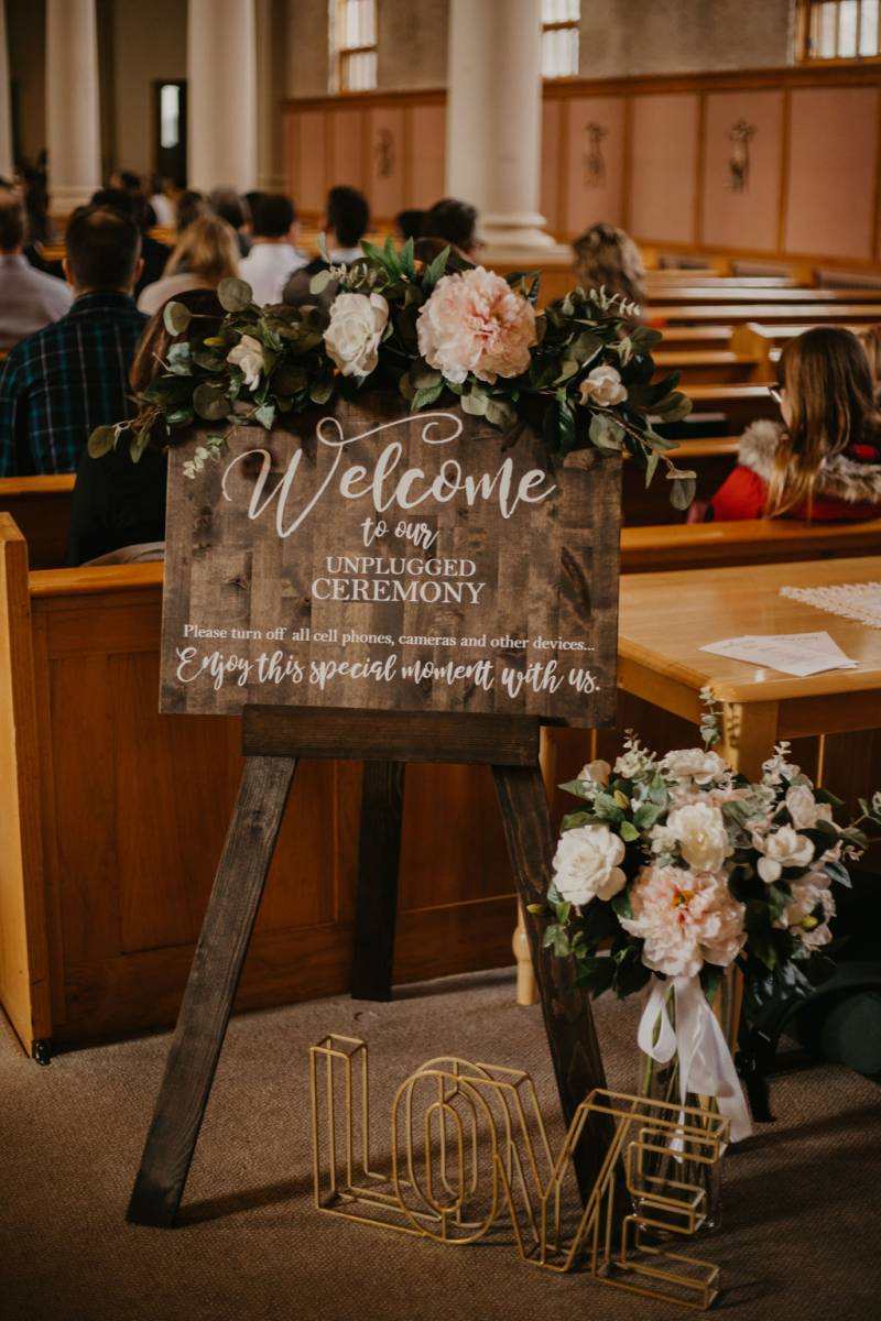 Wedding sign on wooden easel with large blush and white floral accents on top and side 