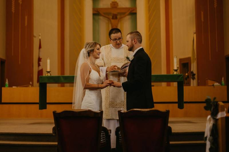 Man and woman standing at front of church holding hands officiant reads behind