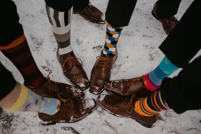 Groom and groomsmen standing with feet together showing multicoloured dress socks on snow