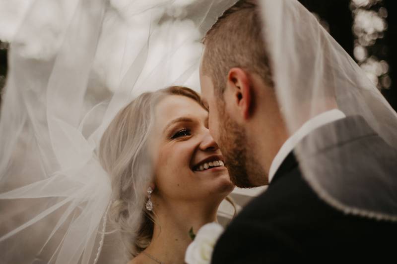 Bride and groom smile looking into eyes while white veil falls overhead