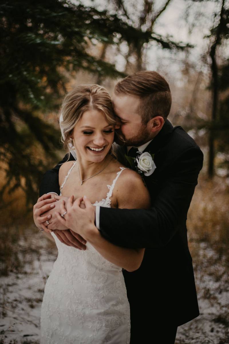 Woman smiles while being embraced by man on light snow forest path