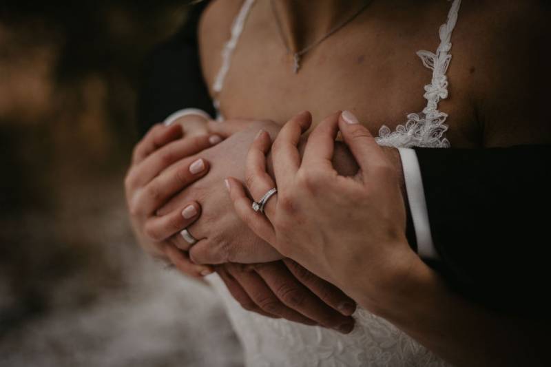 Groom embracing bride from behind with hands showing wedding rings