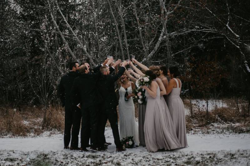 Groomsmen and bridesmaids cheers glasses in a circle on snowy pathway