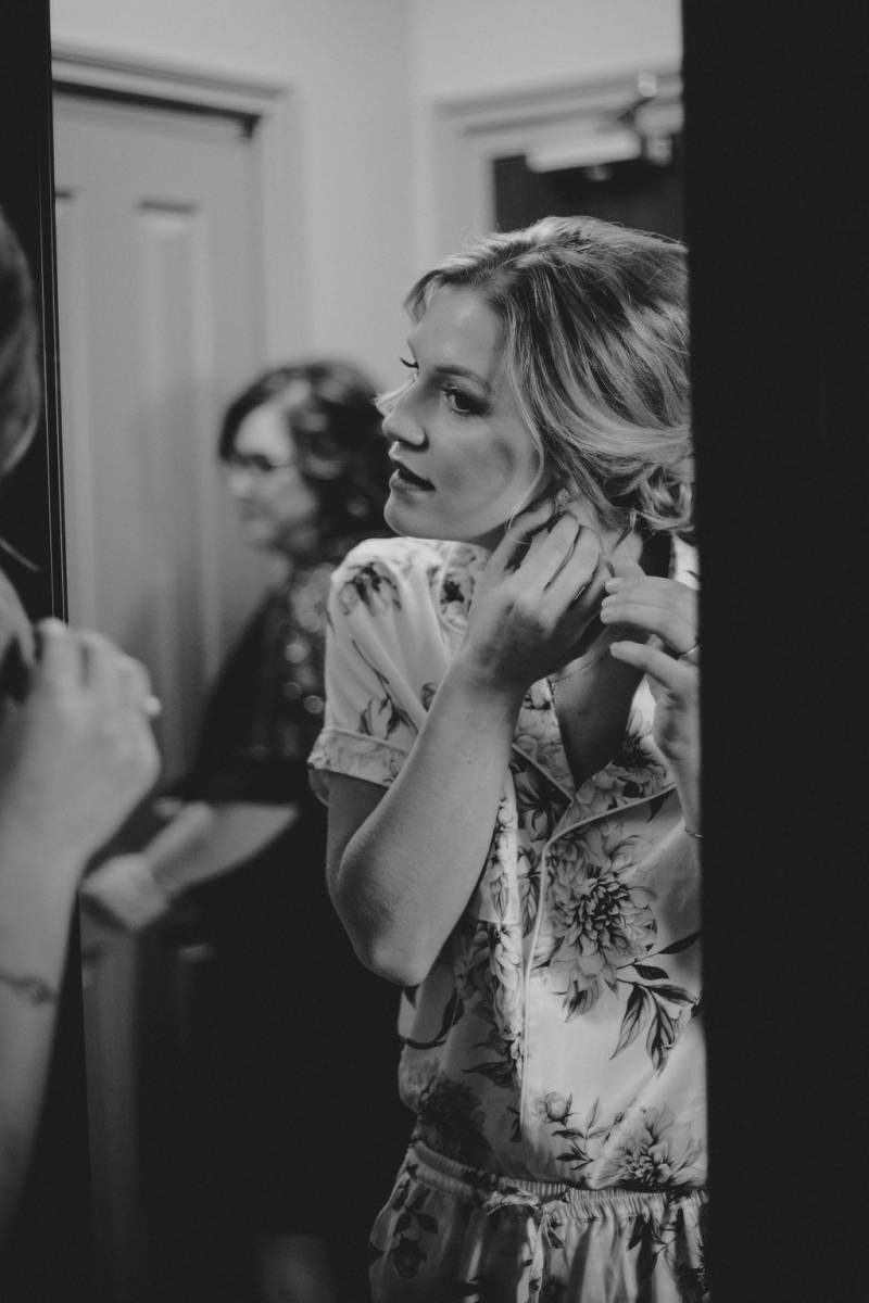 Woman looks into mirror while putting on earrings in floral dress