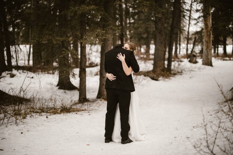 Bride and groom embrace on snowy forest path