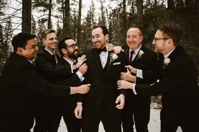 Groomsmen holding grooms arms smiling in snowy forest field 