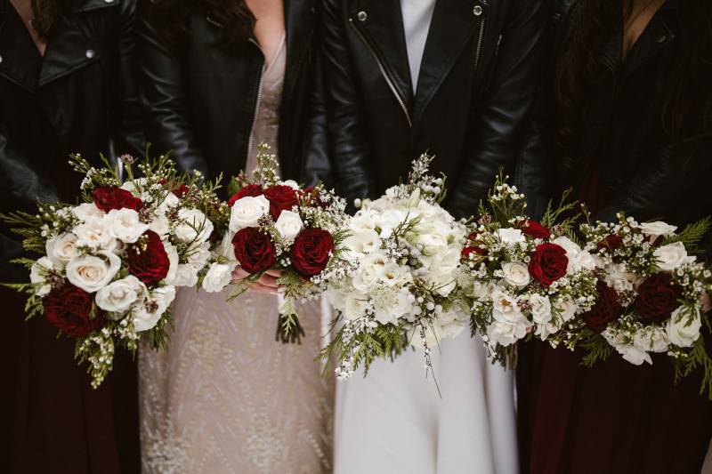 Bride and bridesmaids hold maroon and white bouquets in line 