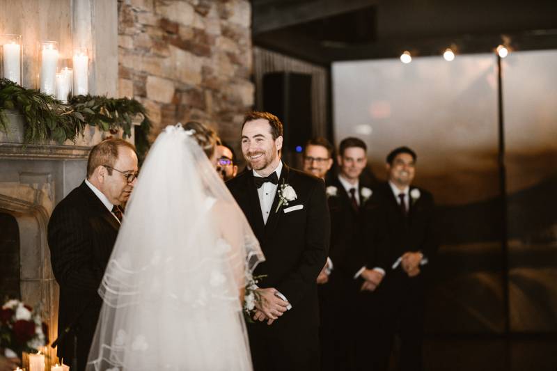 Groom smiling looking at bride in white veil with groomsmen in background