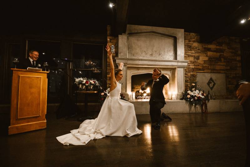 Bride and groom on one knee celebrating in front of podium and fireplace