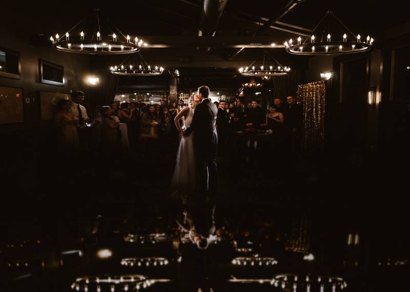 Bride and groom kiss underneath large circle chandeliers 