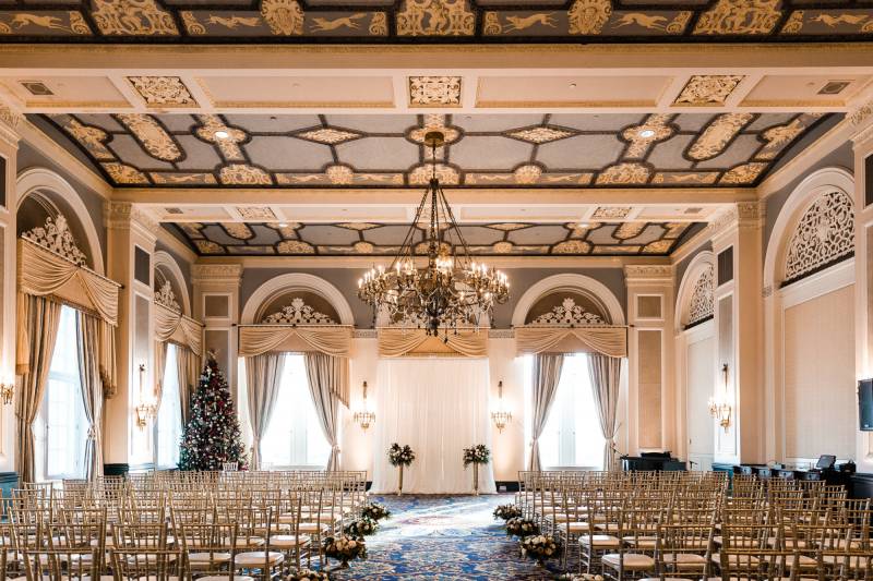 Large wedding venue with cream and gold walls and large hanging chandelier 