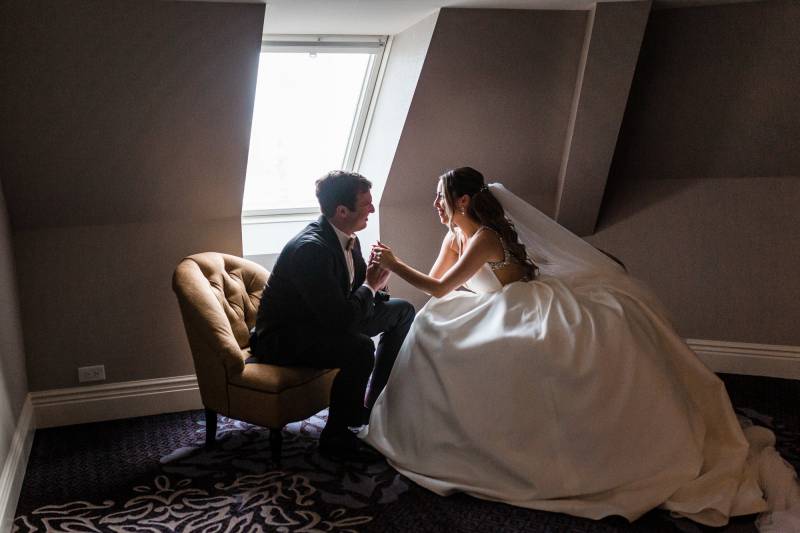 Bride and groom sitting in naturally lit room holding hands 