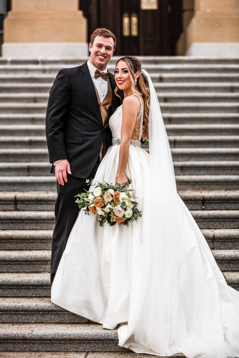 Bride and groom stand on concrete staircase holding peach and white bouquet