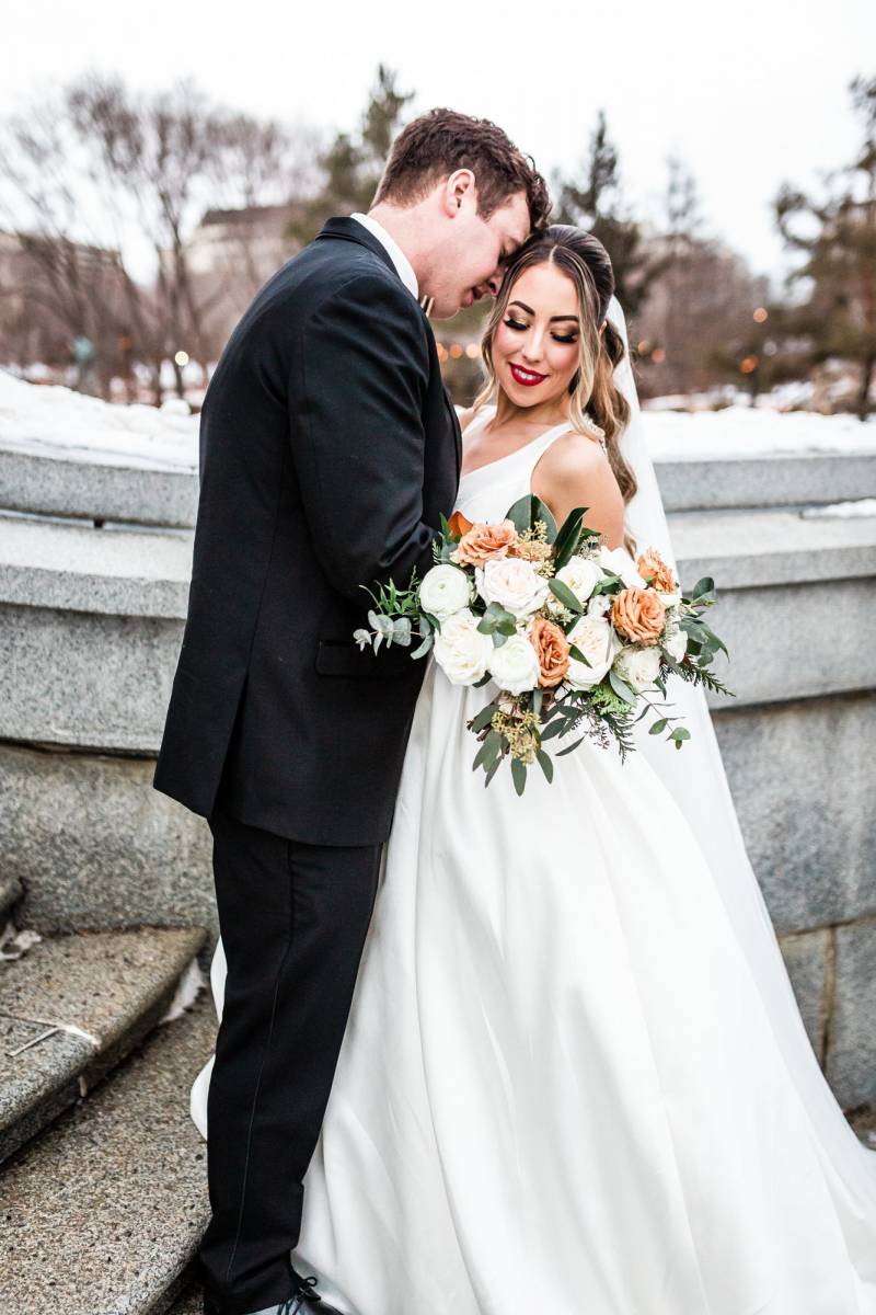 Bride and groom embracing on concrete staircase holding bouquet of peach and white flowers