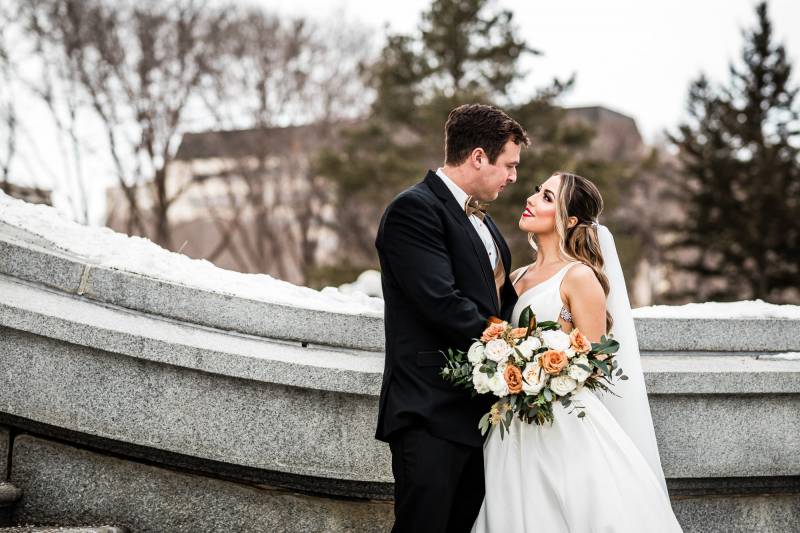 Bride and groom embracing on concrete staircase holding bouquet of peach and white flowers