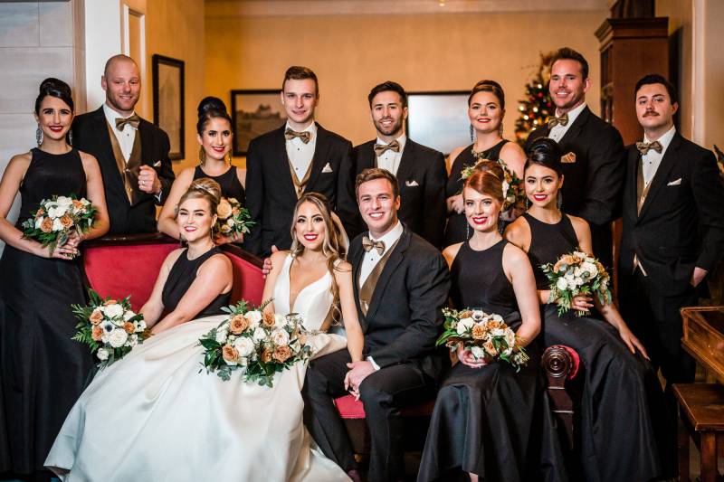 Wedding guests wearing black posing for group photo with bride and groom on red couch 
