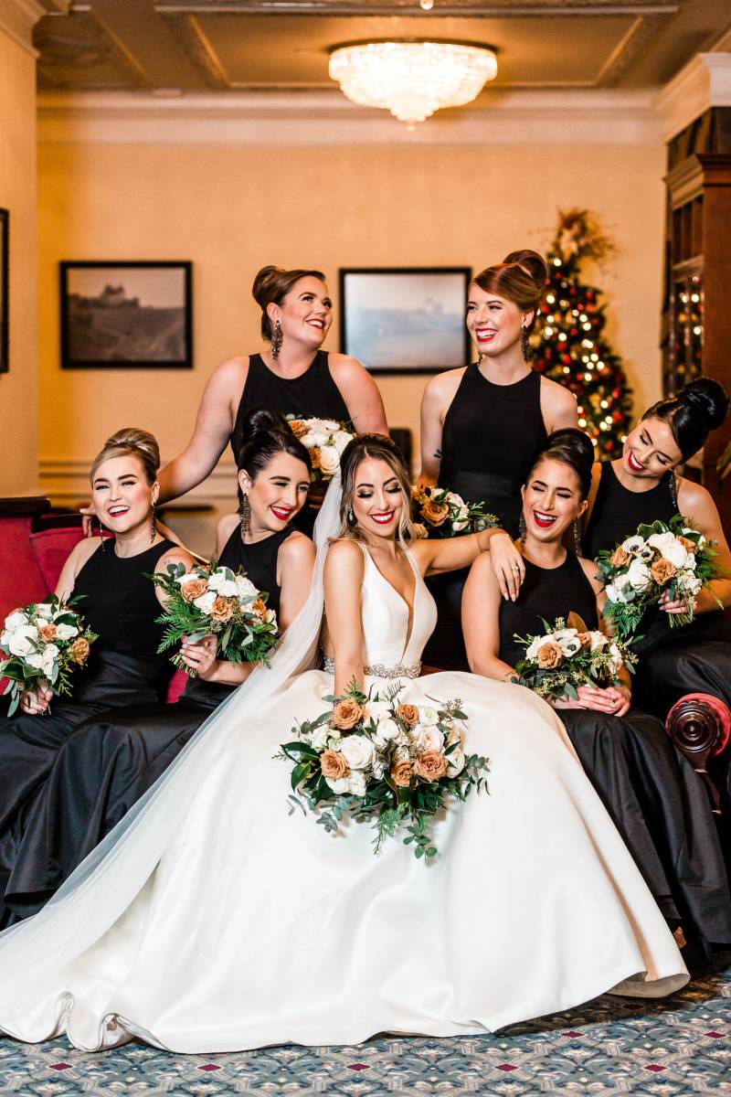 Bride wearing white dress and bridesmaids wearing black dresses holding bouquets 