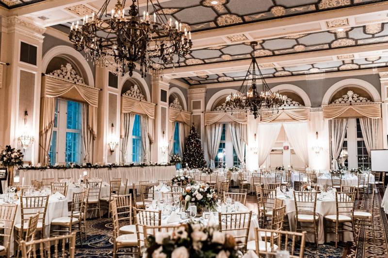 Large room wedding reception with gold chairs and white tan curtains and hanging chandeliers 