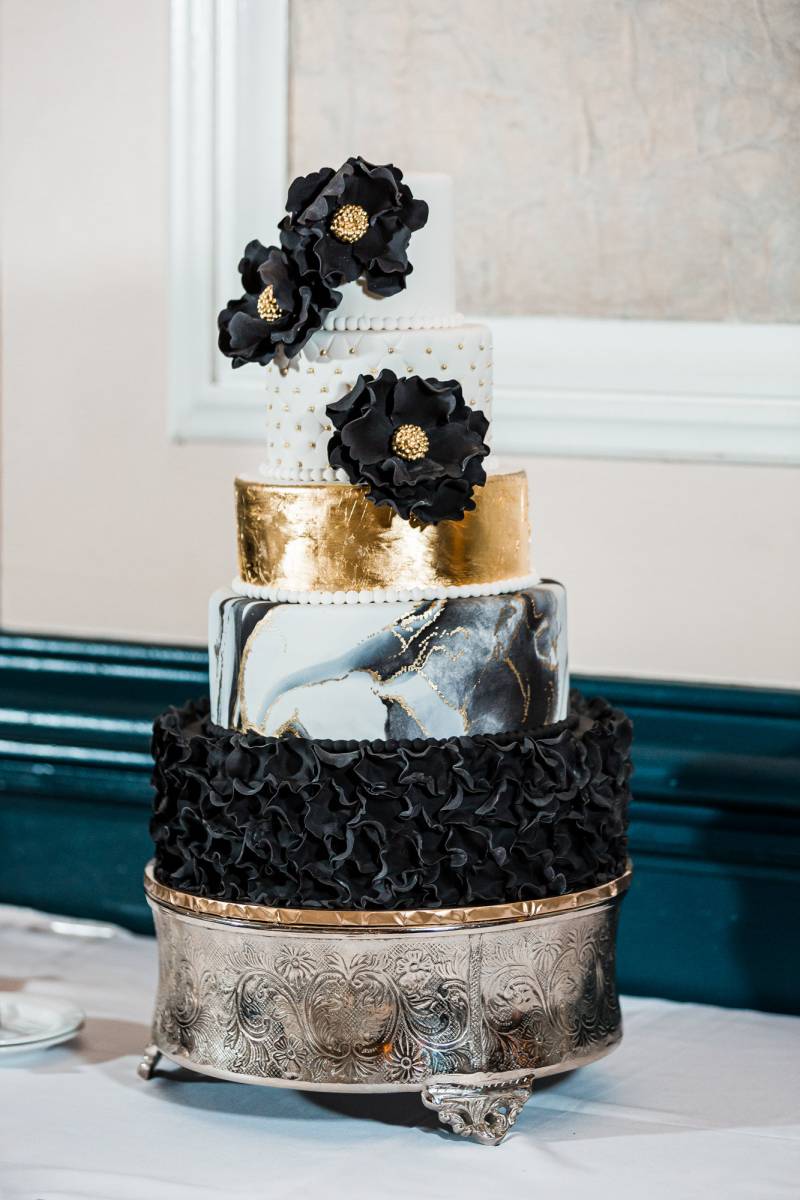 White gold and black four tiered wedding cake with black and gold flowers 
