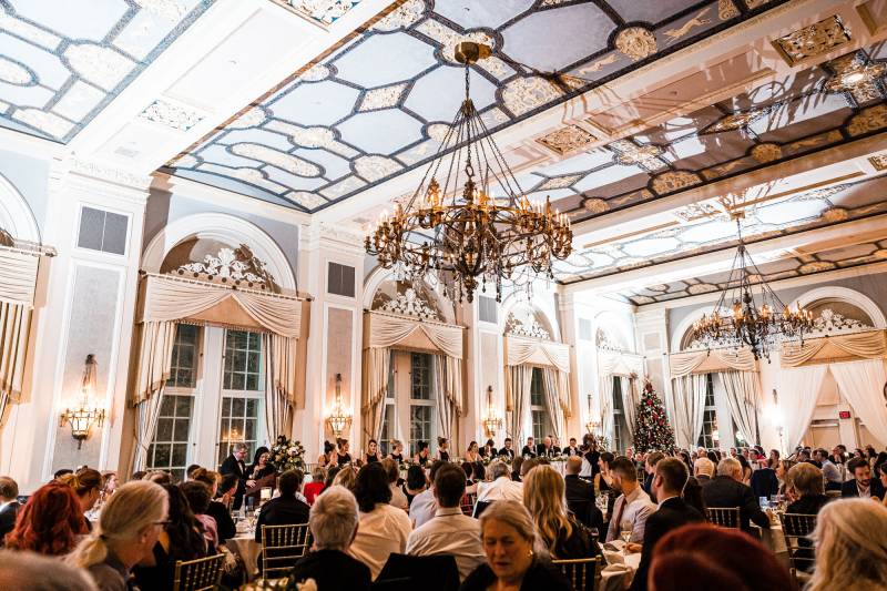 Wedding reception in large room with gold wallpaper and hanging chandeliers 